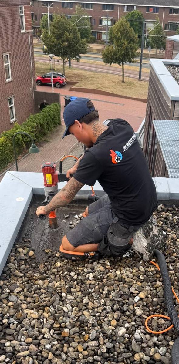 Monteur van BK Montage maakt een kernboring in een plat dak voor de airco-leidingen